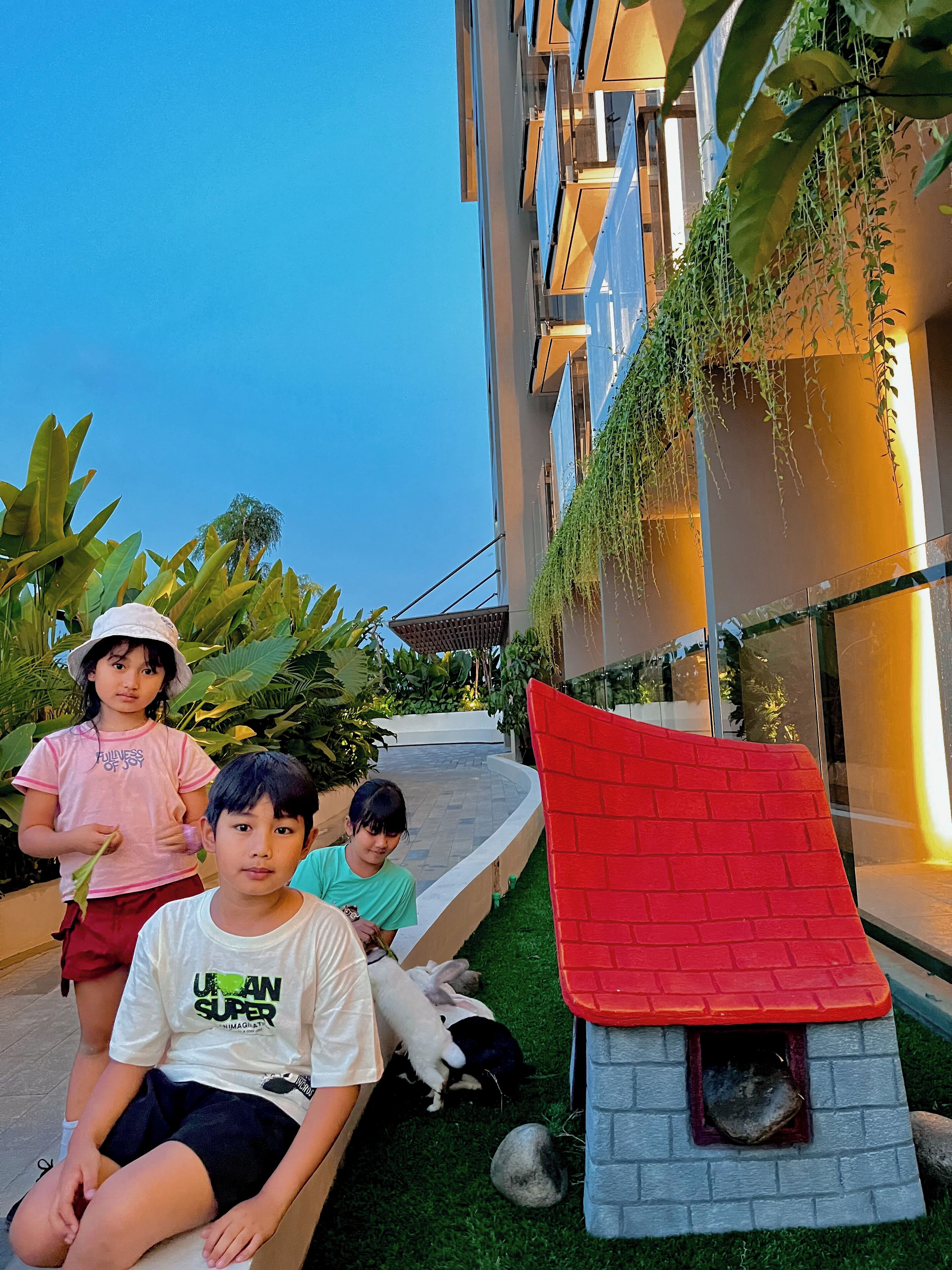 A building with a red-roofed playhouse, green plants, and a clear sky.