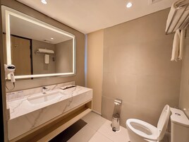 A modern bathroom with a marble sink, a large mirror with lighting, a toilet, and a towel rack.