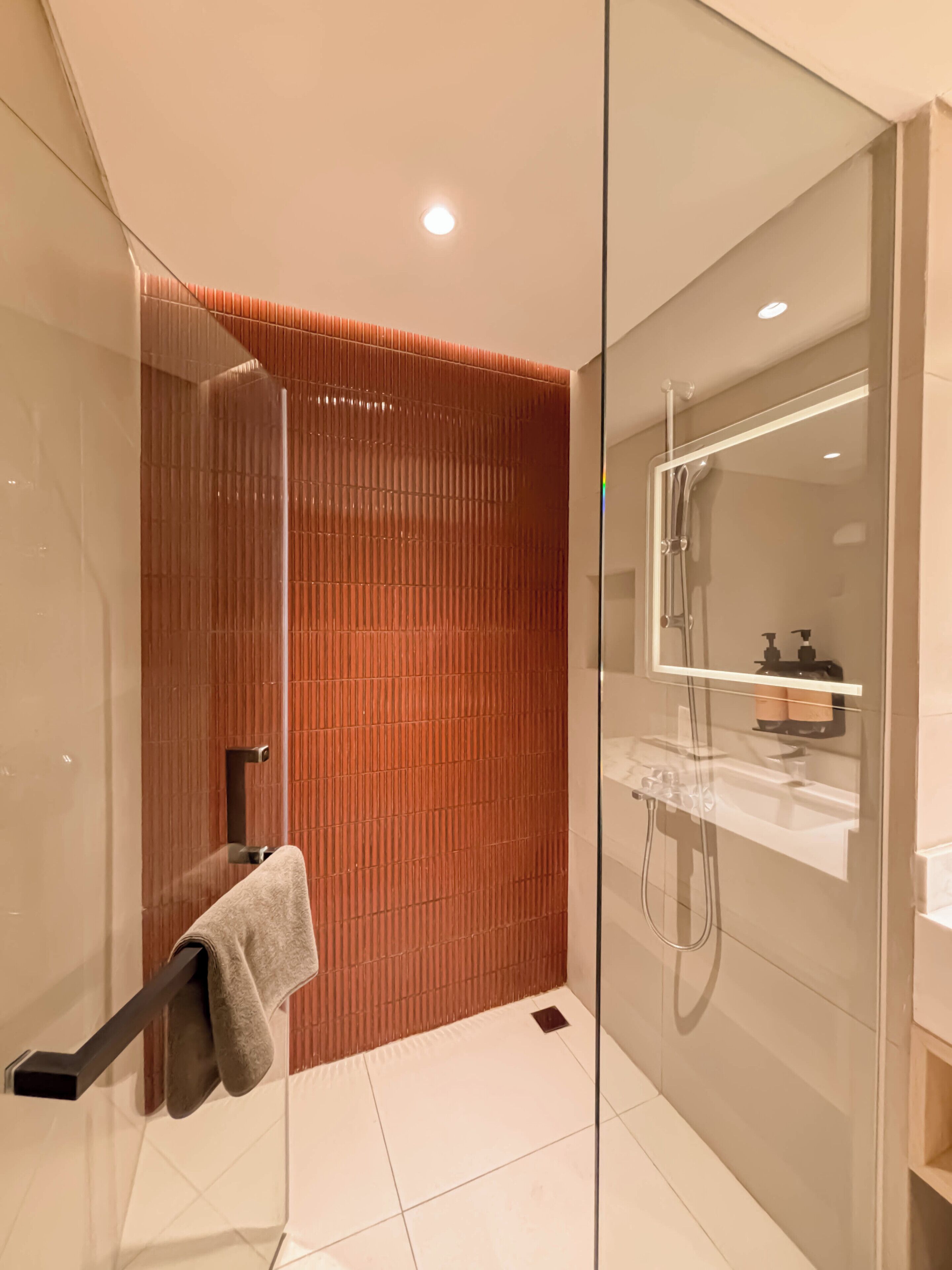 A modern bathroom with a glass shower enclosure, a towel rack, and a wooden accent wall.
