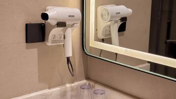 A bathroom with a hairdryer mounted on the wall, a mirror, and two empty glasses on the counter.