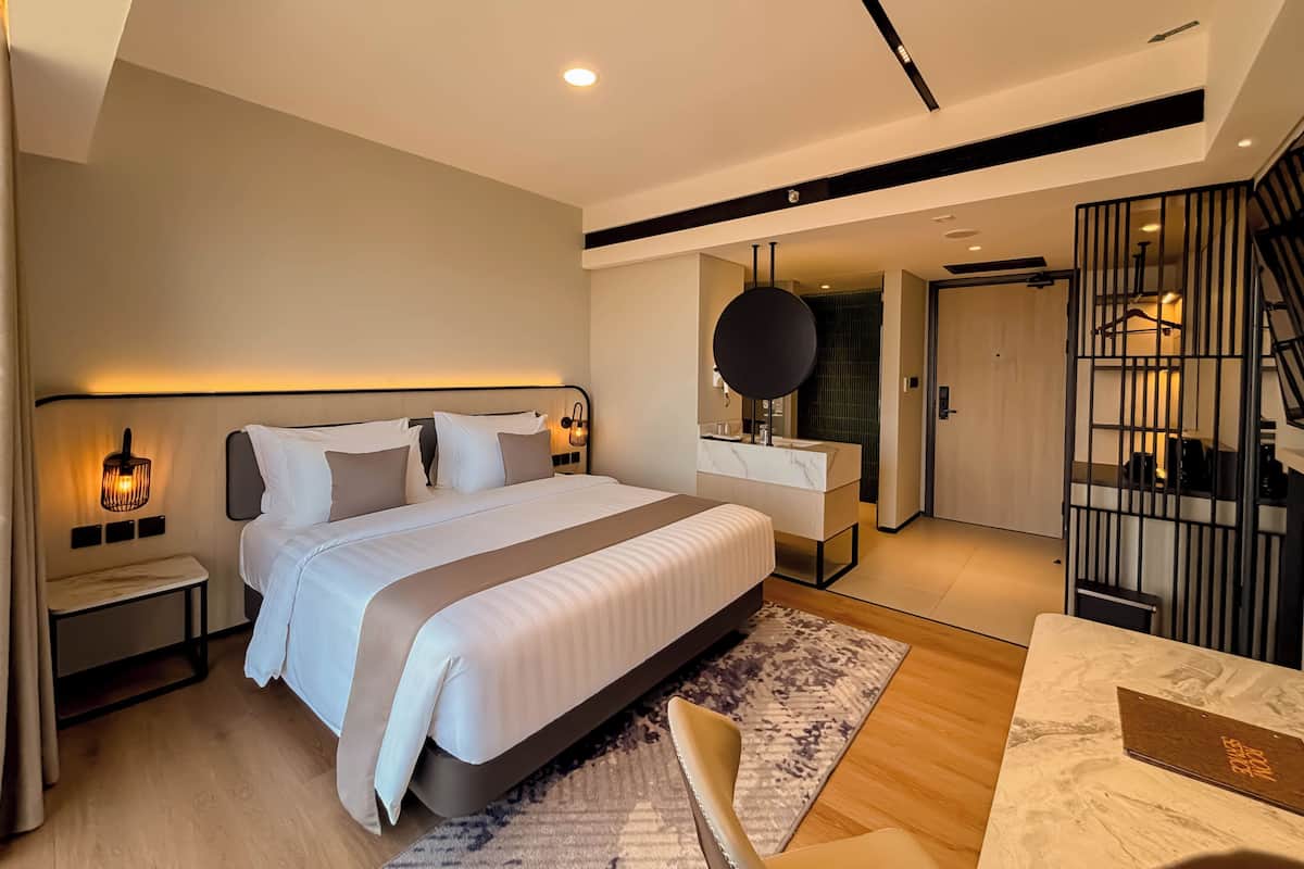 Una habitación de hotel moderna con una cama grande, mesitas de noche, un escritorio y un baño con ducha.