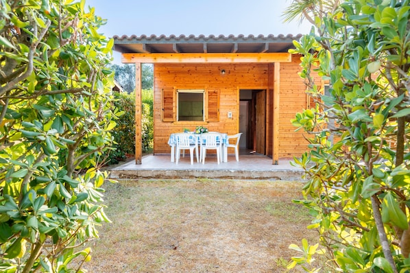 A wooden cabin with a covered patio, a table with chairs, and a door leading inside.