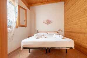 A bedroom with a bed, a wooden ceiling, a wall-mounted picture, and a window with sheer curtains.