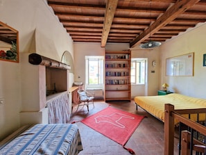 Une pièce avec un plafond en bois, une bibliothèque, un lit recouvert d’une couverture à rayures, un tapis rouge et une chaise.