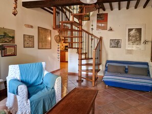 Un salon avec un escalier en bois, un canapé bleu, un fauteuil à motifs et une table basse.
