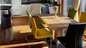 Een moderne keuken met witte kastjes, een eethoek met een houten tafel en gele stoelen, en een uitzicht op de lucht door een raam.