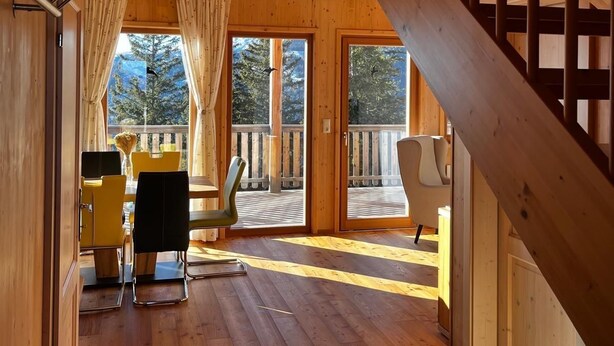 Een houten interieur met een trap, een balkon en een eethoek met gele stoelen en een tafel.