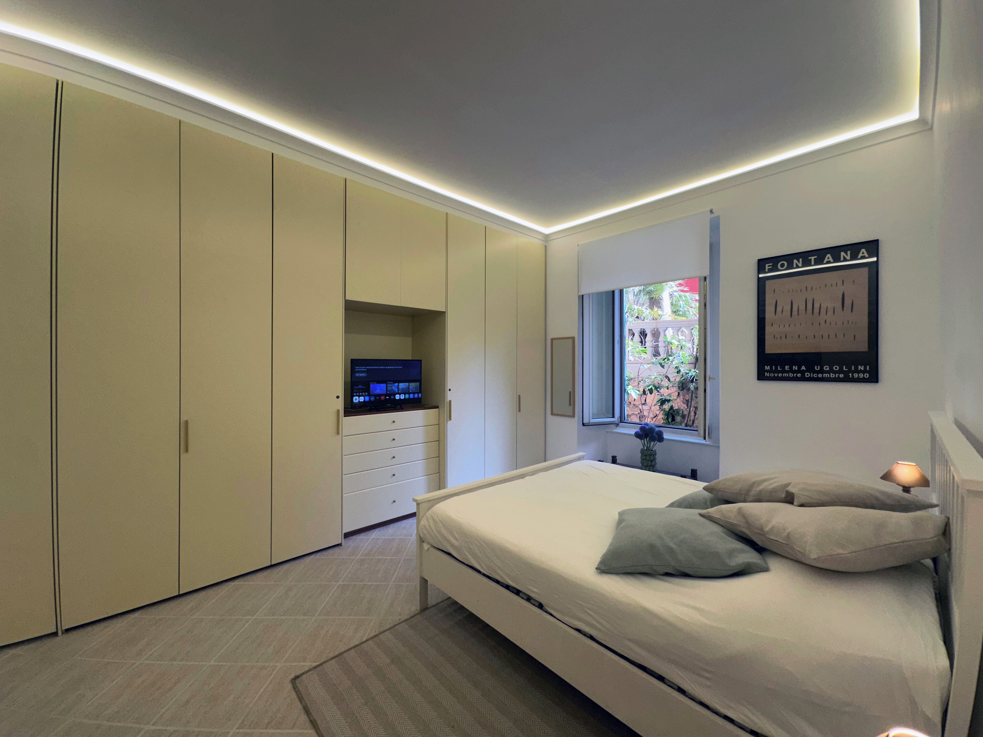 Ein Schlafzimmer mit Bett, Fernseher auf einer Kommode, einem Fenster mit Aussicht und einem gerahmten Bild an der Wand.