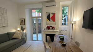 A modern living room with a green sofa, a wooden dining table with chairs, a fireplace, and a TV mounted on the wall. - Villa Borghese Home & Terrace (Roma)
