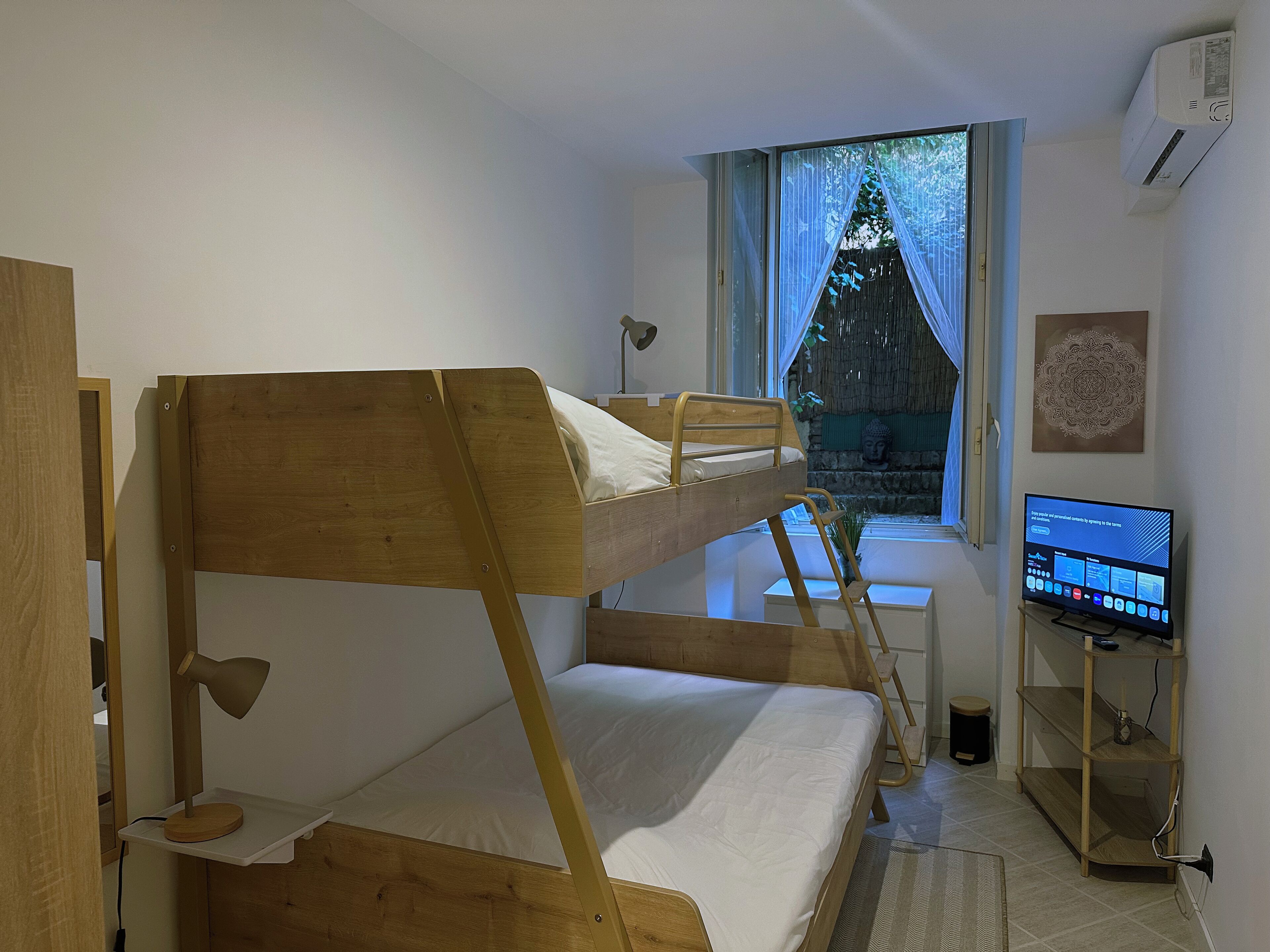 Une chambre avec un lit superposé, un bureau, un ordinateur et une fenêtre donnant sur des arbres.