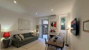 A living room with a sofa, a dining table with chairs, a TV mounted on the wall, and a fireplace. - Villa Borghese Home & Terrace (Roma)