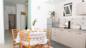 Eine moderne Küche mit Holzschränken, einem Edelstahlkühlschrank und einem Spülbecken. Ein Esstisch mit weißer Spitze und Holzstühle sind ebenfalls vorhanden.