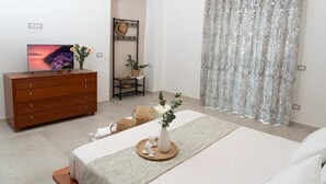 Ein Schlafzimmer mit Bett, Schminktisch, Fernseher, Pflanze und Vorhang.