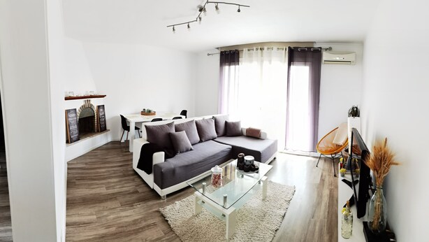 A modern living room with a grey sofa, a glass coffee table, and a dining area with a white table and chairs.