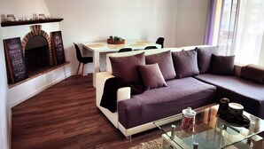 A modern living room with a sofa, a glass coffee table, a fireplace, and a dining area with a table and chairs.