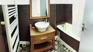 A bathroom with a wooden vanity, a white sink, a mirror, and a bathtub.