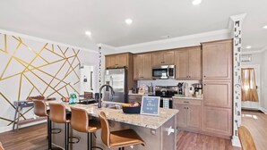 A modern kitchen with a central island, bar stools, wooden cabinets, stainless steel appliances, and a chalkboard sign. - 4 King Beds - 2 Game Rooms - Sleeps 24, By DT & UGA (Athens)