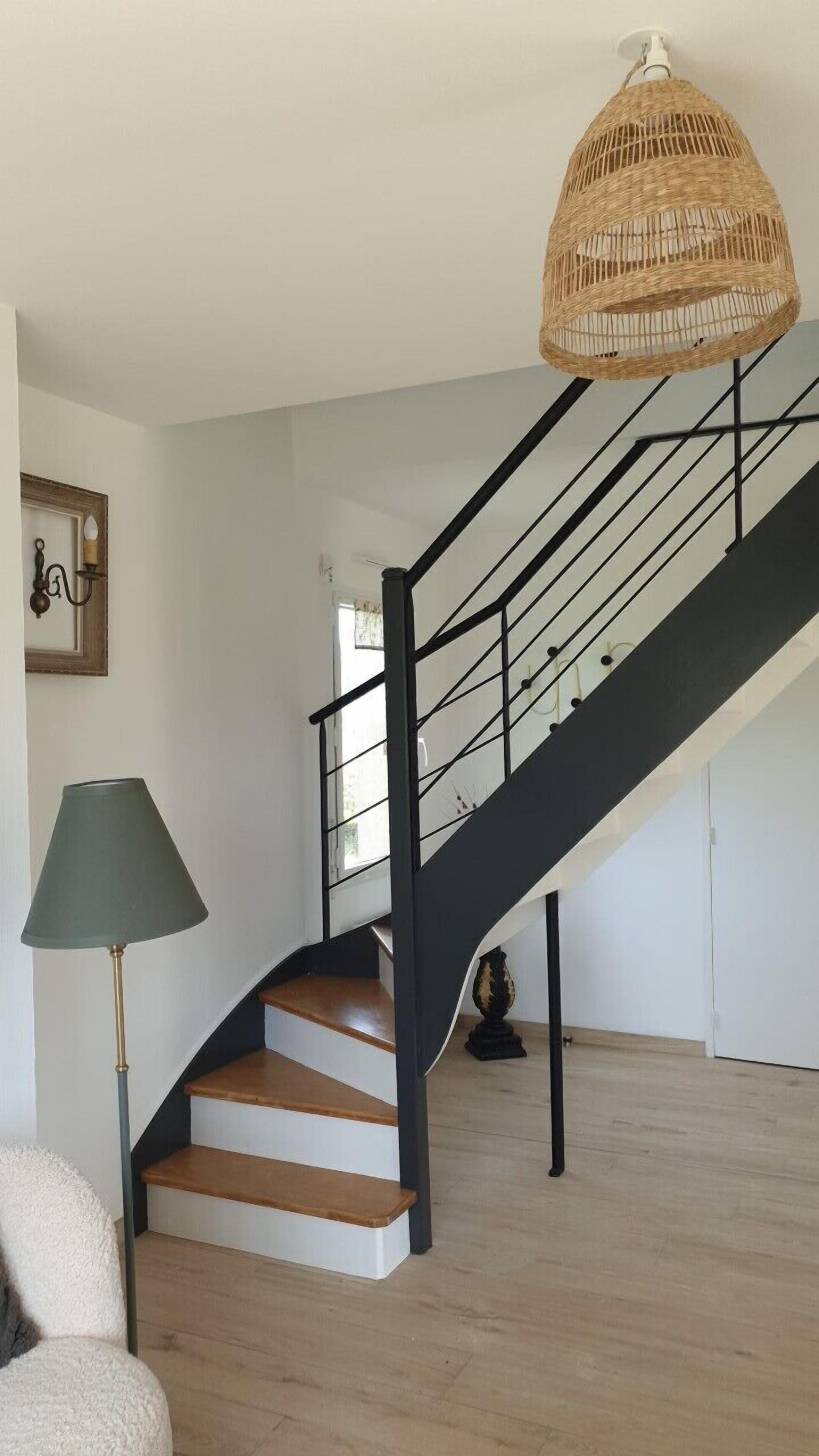 A staircase with a black railing and a woven light fixture above it.