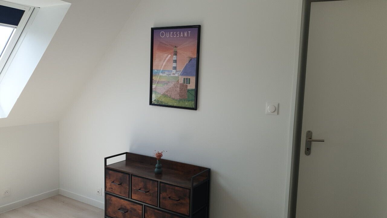 A room with a sloped ceiling, a wooden dresser with drawers, a framed picture on the wall, and a door.