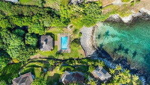 Vue aérienne d’une propriété située sur la côte, avec une piscine, une végétation luxuriante et une côte rocheuse.