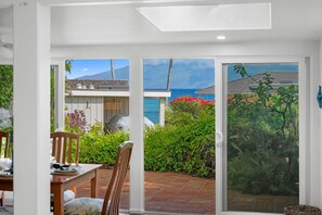 A room with a sliding glass door leading to a patio with a view of the sea and a mountain.
