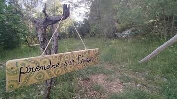Un letrero de madera con un diseño decorativo y el texto 'Prendre son temps' colgado de un árbol en una zona verde.