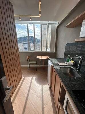 A modern kitchen with a large window, wooden flooring, and a built-in oven. - 14m2 | 32" TV | Near beach | Near mall 24A (Rio de Janeiro)