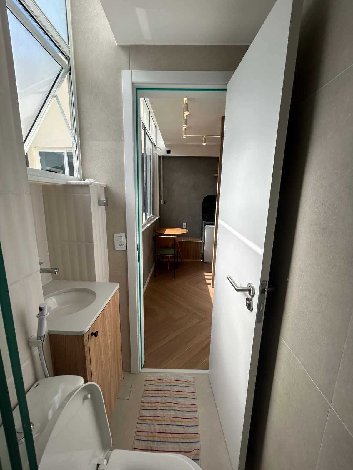 Une salle de bain moderne avec un lavabo, des toilettes et une douche. On aperçoit un petit coin repas à l’arrière-plan.