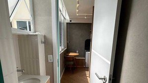 Een moderne badkamer met een wastafel, toilet en douche. Achtergrond toont een klein zithoekje.