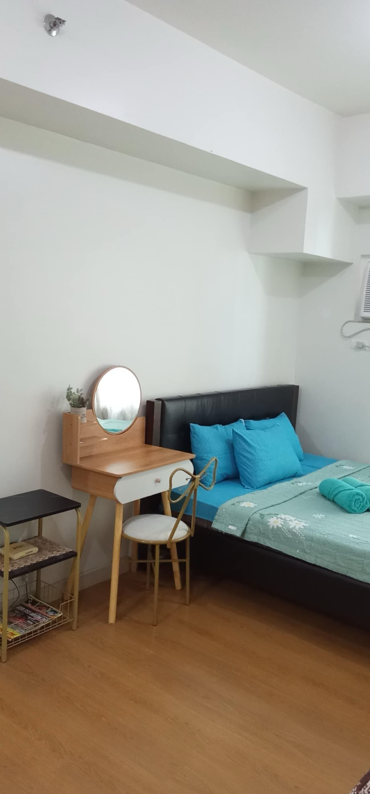 A bedroom with a bed, a desk with a chair, a small table, and a mirror.