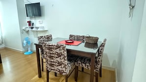Un coin repas avec une table et des chaises, un téléviseur fixé au mur, un téléphone et un ventilateur.