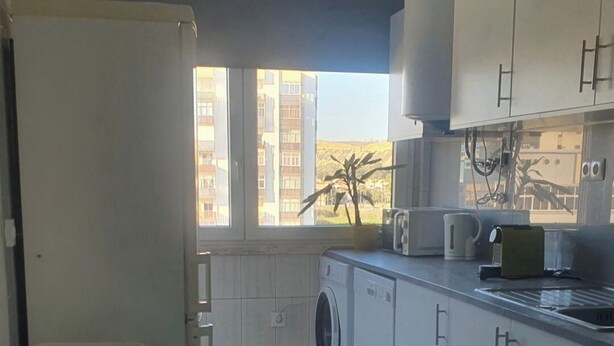 A compact kitchen with a washing machine, a dining table, and a view of high-rise buildings through the window.