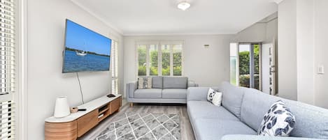 Ett modernt vardagsrum med en grå soffa, en platt-TV och en möbel i trä för underhållningsutrustning.