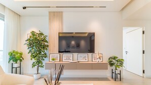 Ein modernes Wohnzimmer mit einem an der Wand befestigten Flachbildfernseher, einer Couch und Topfpflanzen.