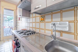 Une cuisine équipée d’une cuisinière à gaz, d’un évier en acier inoxydable et offrant une vue sur l’extérieur.