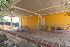 A covered patio area with a table and chairs, a stone floor, and a yellow wall.