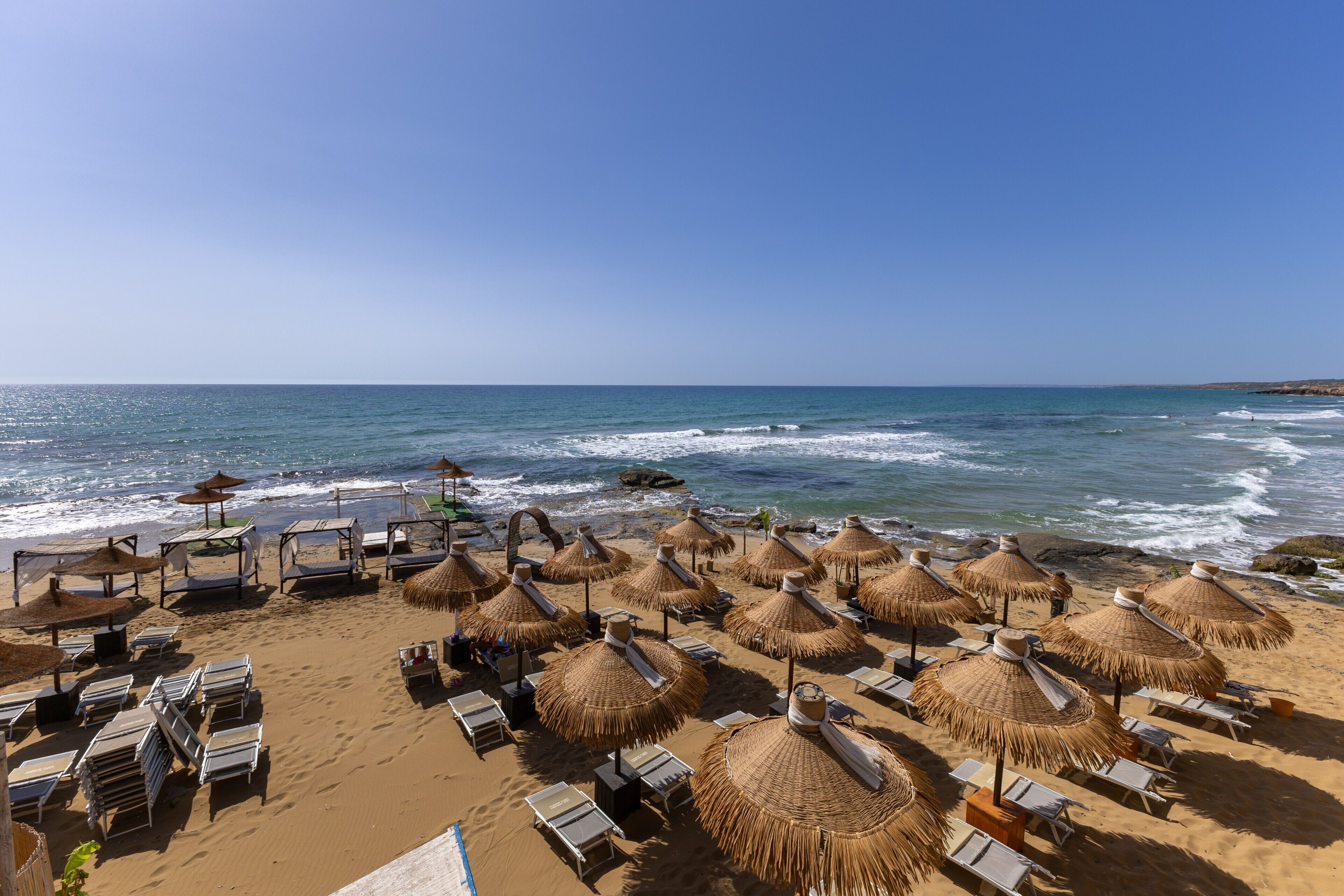 Une plage avec des chaises longues et des parasols en chaume.