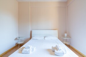 Un lit bien fait, avec du linge de lit et des serviettes blanches, deux tables de chevet avec des lampes et un mur sobre.