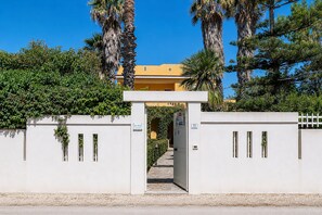Une entrée fermée par un portail, avec un chemin dégagé menant à un bâtiment à la façade jaune.