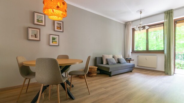 A modern living room with a dining area, a sofa, and a large window with curtains.