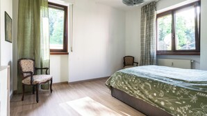 A bedroom with a bed, two chairs, a window with curtains, and a radiator.