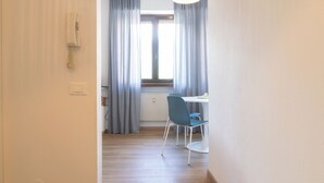 A hallway leading to a room with a window, curtains, a telephone, and a table with chairs.