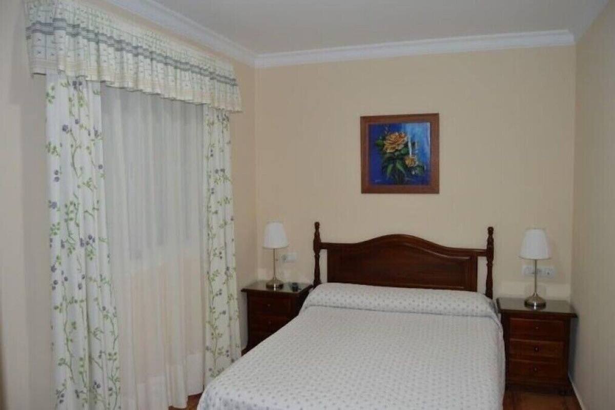 A bedroom with a wooden bed, two bedside tables with lamps, a floral curtain, and a painting on the wall.