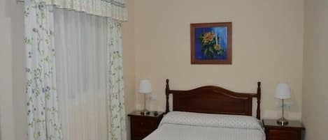 Une chambre à coucher avec un lit en bois, deux tables de chevet avec des lampes, un rideau à motifs floraux et un tableau au mur.