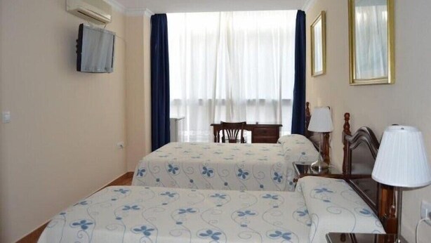 Une chambre d’hôtel avec deux lits, un bureau, une chaise et un téléviseur fixé au mur.