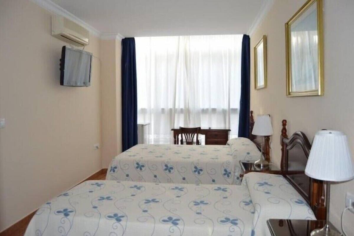 A hotel room with two beds, a desk, a chair, and a TV mounted on the wall.