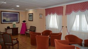 Habitació d'hotel amb una finestra gran, un quadre a la paret, una cadira, un taulell i una làmpada.