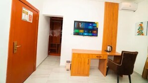 A room with a wooden desk, a chair, a television mounted on the wall, and a wardrobe. - The Harmony Oasis Hotel and Suites (Port Harcourt)