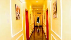 A brightly lit hallway with yellow walls and red doors, leading to a room with a large bed and a nightstand. - The Harmony Oasis Hotel and Suites (Port Harcourt)