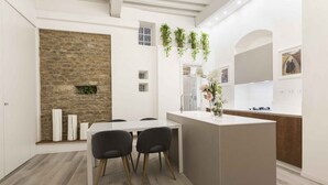 Une cuisine moderne avec un mur d’accent en pierre, un coin repas avec une table et des chaises blanches, et un petit îlot central doté d’un évier.